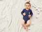 Un bébé dans un body bleu avec un imprimé lapin, allongé sur une couverture tricotée.