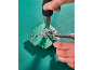Mains réparant une carte de circuit imprimé avec un pistolet à air chaud et une pince sur un tapis de découpe.