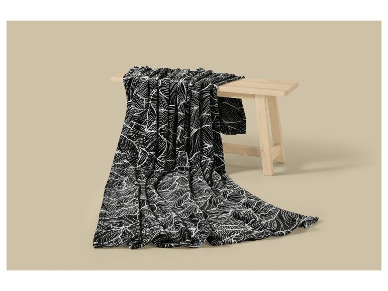 Plaid noir à motif de feuilles blanches sur un banc en bois.