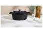 Cocotte en fonte noire avec couvercle, moulins à poivre et à sel en bois sur un comptoir en marbre.