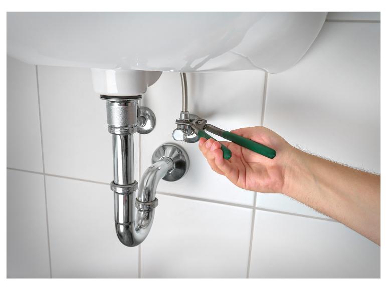 Une main utilise une pince pour réparer un robinet sous un lavabo.