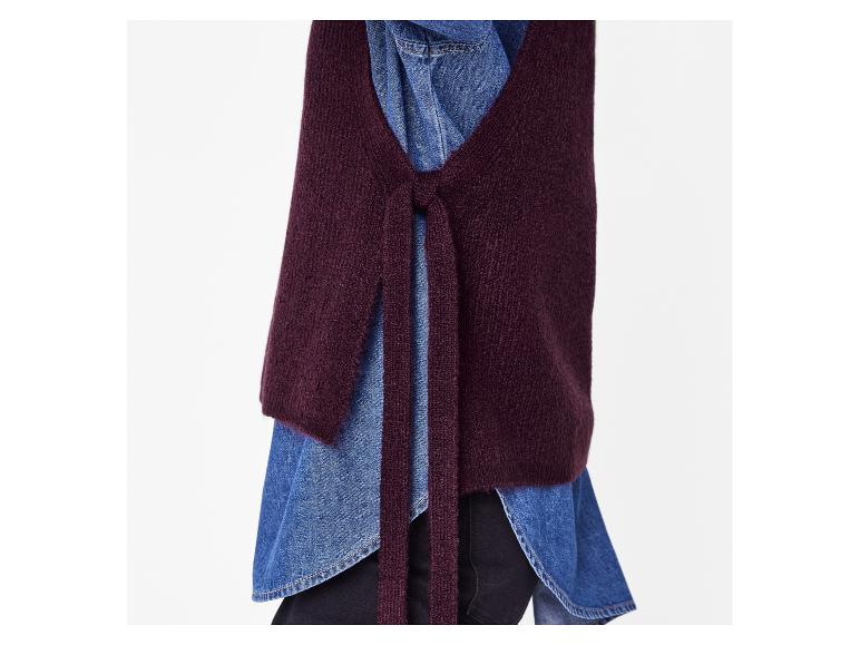 Gros plan d'un gilet en maille bordeaux noué sur une chemise en jean bleue.