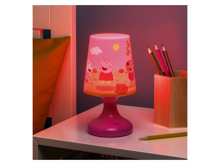 Lampe d'enfant rose avec des personnages de dessins animés et un pot de crayons de couleur sur une table.