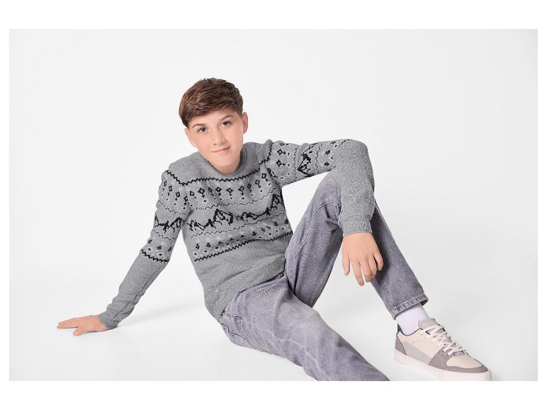 Garçon en pull tricoté gris à motifs et jean gris assis par terre.