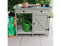 Banc de jardin avec arrosoir, pots et un sac de terre.