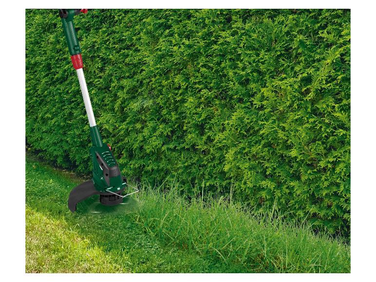 Coupe-bordures tond l'herbe haute près d'une haie.