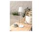 Lampe de table blanche moderne sur une table en bois, près d'un fauteuil en rotin.