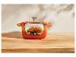 Un poulet rôti dans une cocotte Le Creuset orange sur une table en bois.