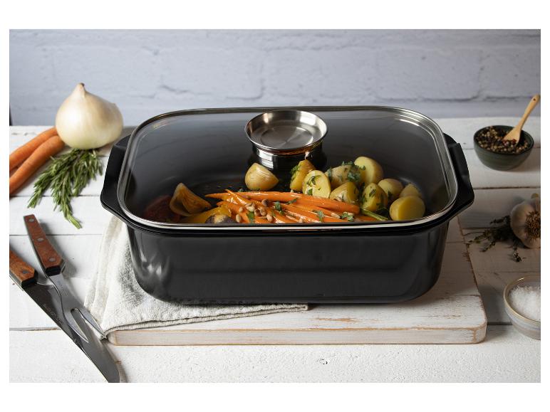Rôtissoire noire avec couvercle en verre, remplie de légumes rôtis, sur une planche en bois.