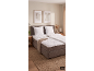 Chambre avec un lit double gris, de la literie blanche, un tapis en jute et des tableaux abstraits.