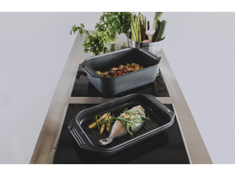 Deux plats à rôtir noirs avec du poisson et des légumes sur une plaque à induction