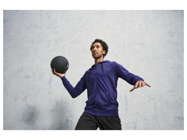 Un homme dans un sweat-shirt à capuche bleu tient un ballon d'entraînement.