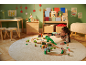 Fille jouant avec un train en bois et des dinosaures sur un tapis rond dans une pièce décorée pour Noël.