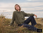 Femme en veste verte et jean foncé assise dans un champ d'herbe.