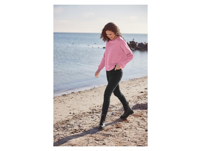 Une femme porte un pull rose, un jean noir et des bottes sur la plage.