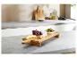 Planche de service en bambou avec fromage, raisins et olives sur un comptoir de cuisine.