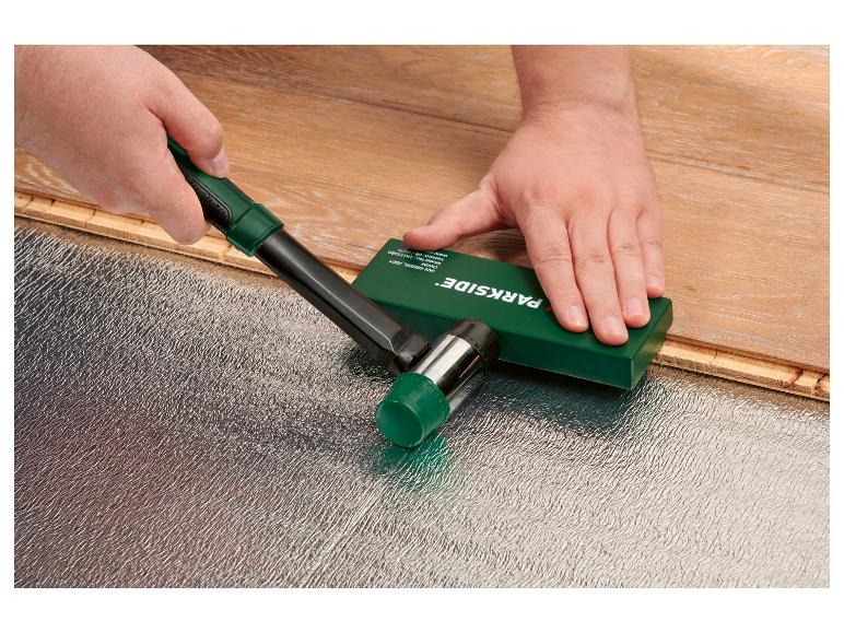 Un ouvrier installe un revêtement de sol stratifié avec un maillet en caoutchouc et une cale de frappe.