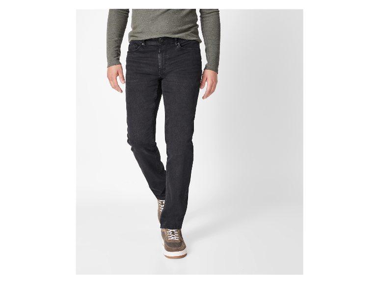 Un homme porte un jean noir et un pull vert olive.