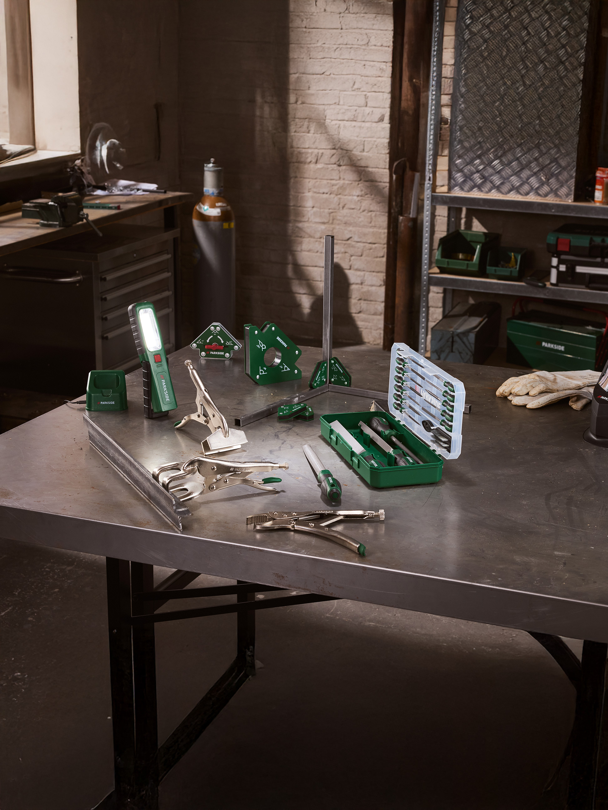Outils de soudage et de limage sur une table métallique dans un atelier, avec une lampe de poche LED.