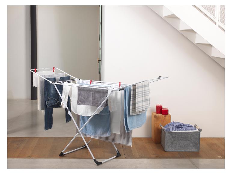 Séchoir à linge blanc avec du linge étendu, un panier à linge et des bougies rouges.