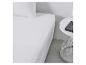 Draps blancs sur un lit avec une table de chevet blanche.
