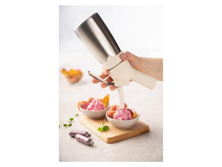 Siphon à crème fouettée remplissant de la crème rose dans un bol de fruits, avec des cartouches.