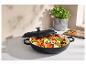 Cocotte noire avec couvercle, remplie de légumes coupés, sur un comptoir avec un plant de basilic.