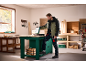 Homme dans un atelier de menuiserie, ouvrant une boîte à outils sur un établi vert.