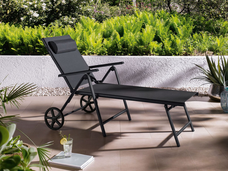 Un transat noir avec des roues et un repose-pieds assorti dans un jardin.