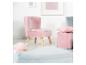 Fauteuil enfant en velours rose avec pouf et coussin assortis dans une pièce lumineuse.
