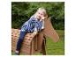 Fille blonde assise sur un cheval jouet en bois à l'extérieur.
