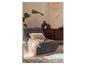 Un fauteuil lounge gris avec un coussin et un plaid crème, à côté d'un meuble en bois.