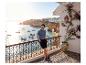 Homme en polo et short sur un balcon avec vue sur la mer et les bateaux.