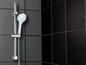 Une pomme de douche et une barre chromées contre un mur de carreaux noirs.