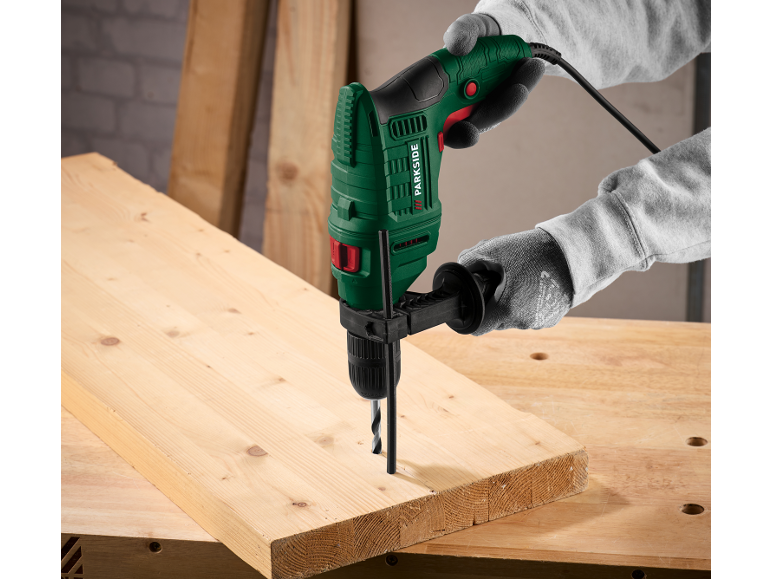 Perceuse à percussion dans les mains, perçant une planche de bois sur un établi.