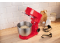 Robot pâtissier rouge avec pâte dans un bol, ingrédients de cuisson et accessoires sur un comptoir en bois.
