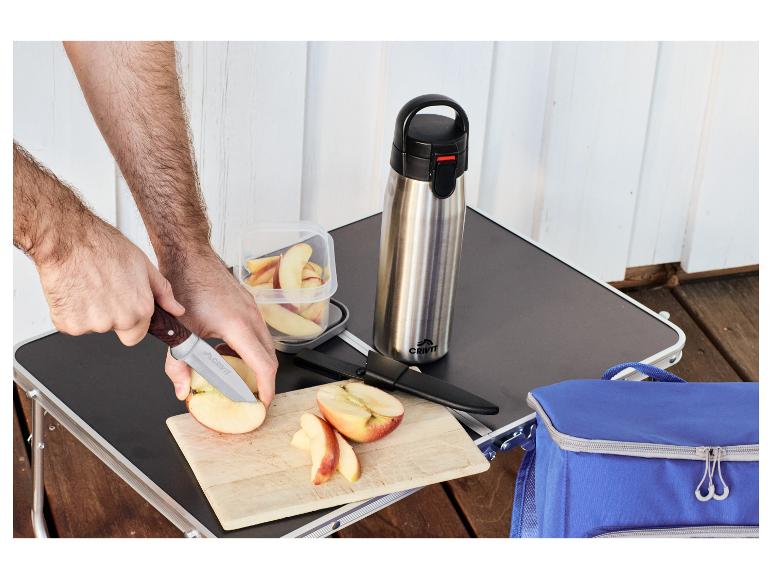 Homme coupant des pommes sur une table de pique-nique avec une bouteille isotherme et un sac glacière.