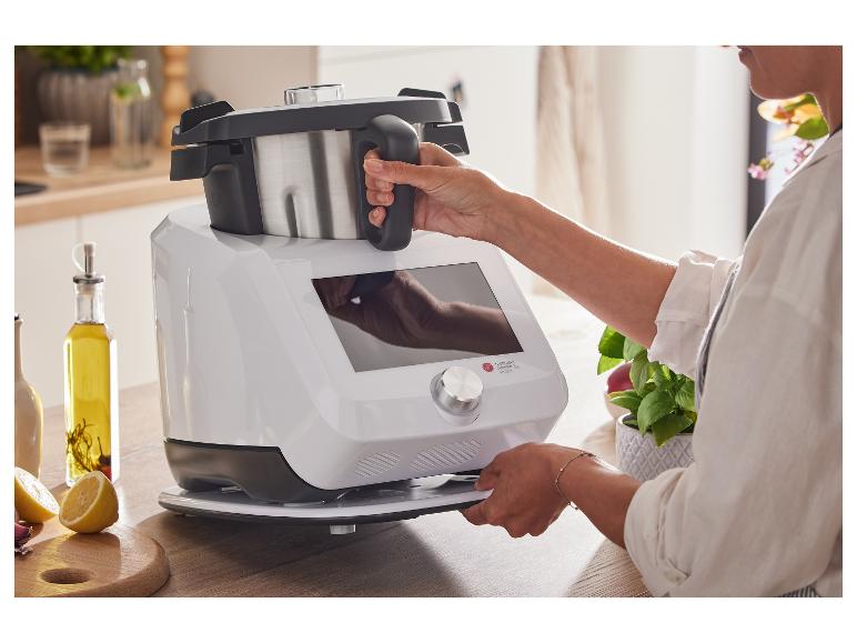 Femme utilisant un robot de cuisine blanc avec bol en acier inoxydable dans une cuisine lumineuse.