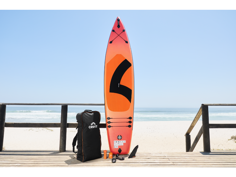Paddleboard orange avec accessoires et sac sur une promenade en bois au bord de la plage.