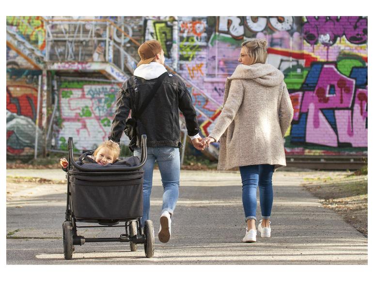 Famille avec enfant en poussette se promène main dans la main le long d'un mur de graffitis.