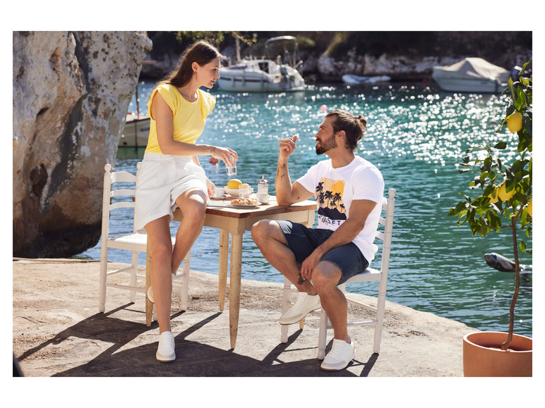 Un homme et une femme portant des baskets blanches et des vêtements d'été décontractés, assis à une table au bord de l'eau.