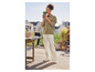 Une femme porte une veste verte, un pantalon blanc et des baskets blanches sur une terrasse.