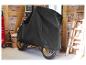 Une moto recouverte d'une housse noire dans un garage.