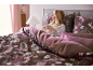 Femme au lit avec une parure de lit florale, buvant du thé.