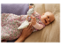 Bébé souriant dans une gigoteuse à fleurs jouant avec un hochet en bois.