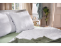 Oreillers et couette matelassés blancs sur un lit avec des draps et une couverture verts.
