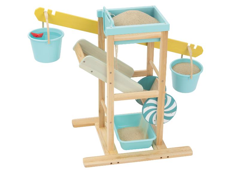 Station de jeu en bois pour sable et eau avec seaux, sable, eau et un bateau en papier rouge.