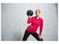 Une femme portant un sweat-shirt rose et un pantalon noir tient un ballon d'entraînement.