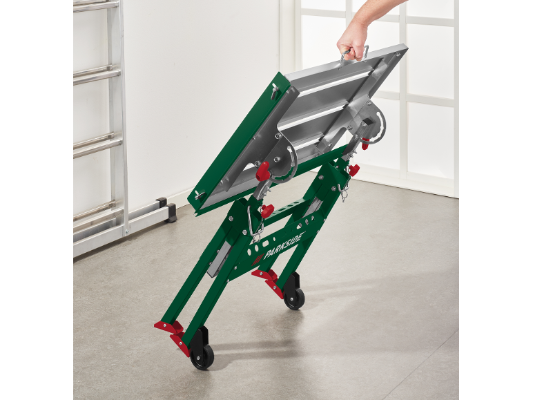 Support de travail pliable à roulettes, tenu par une main, avec une échelle en arrière-plan.