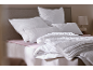 Literie et oreillers blancs à motifs sur un lit avec un drap rose.